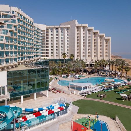 Leonardo Club Hotel Dead Sea Neve Zohar Exterior photo The image shows a large hotel complex alongside a pool area. The hotel features modern architecture with multiple levels and numerous balconies. In front of the hotel, there is a recreational area with a swimming pool, water slides, and lounging chai