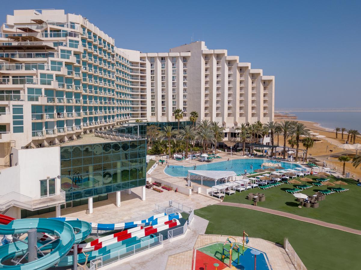 Leonardo Club Hotel Dead Sea Neve Zohar Exterior photo The image shows a large hotel complex alongside a pool area. The hotel features modern architecture with multiple levels and numerous balconies. In front of the hotel, there is a recreational area with a swimming pool, water slides, and lounging chai